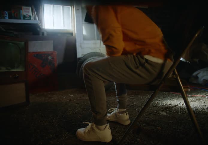 A man takes a seat in a metal folding chair in a small shack with a dirt floor