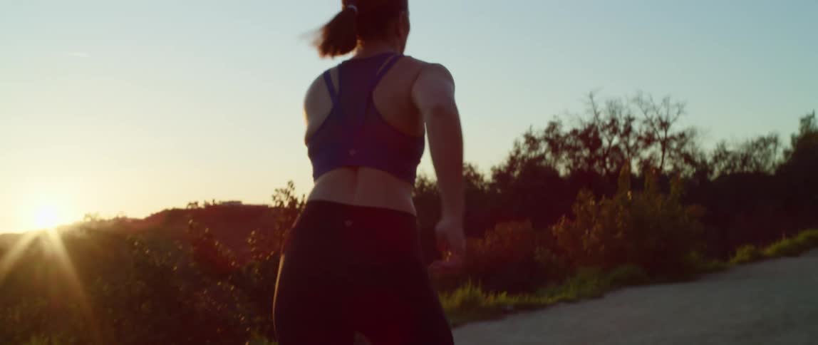A woman jogs along a dirt road up a large hill on a clear day