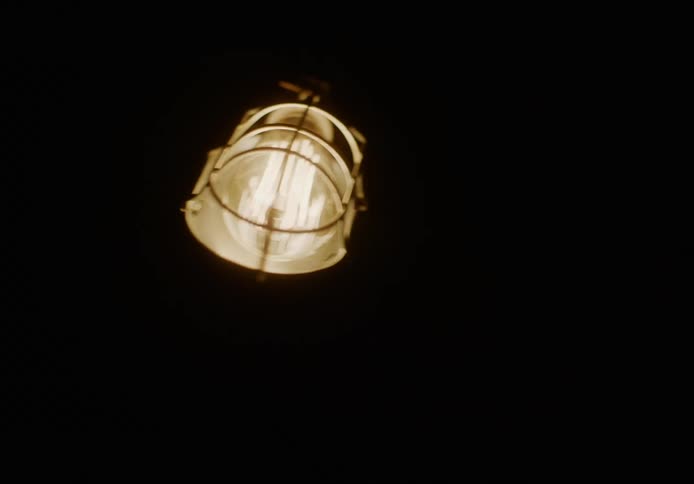 A lighted drop lamp swings back and forth in a dark room