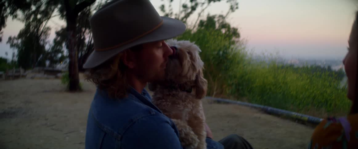 A man lifts his dog off the picnic blanket