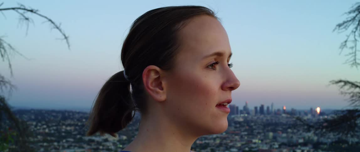Side view of a woman with a ponytail breathing deeply and looking out over the city skyline at dusk