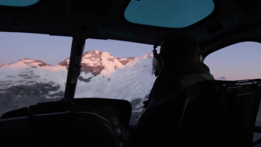 Two people flying a helicopter over a mountain range