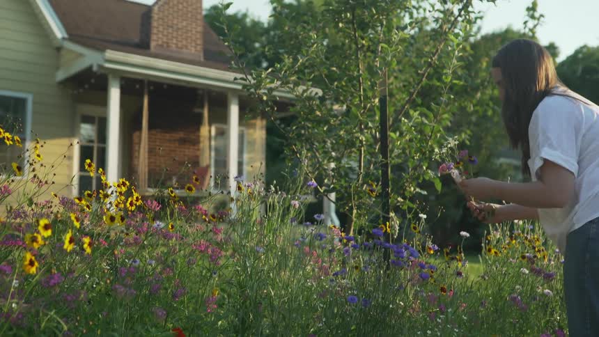 A young woman cuts flowers outside her home