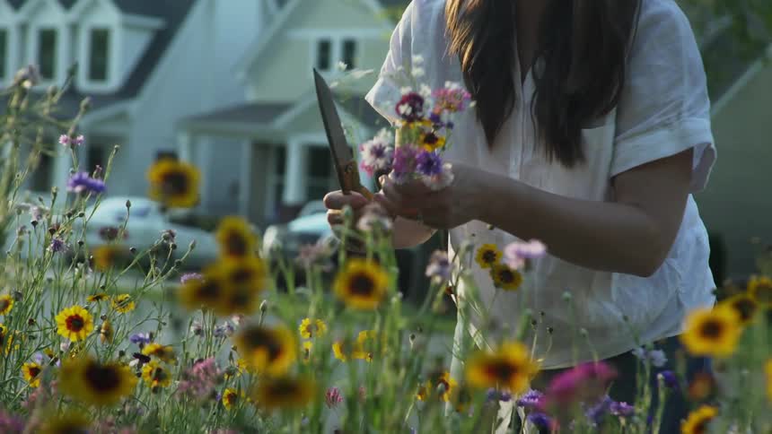 A young woman gathers flowers from her front yard
