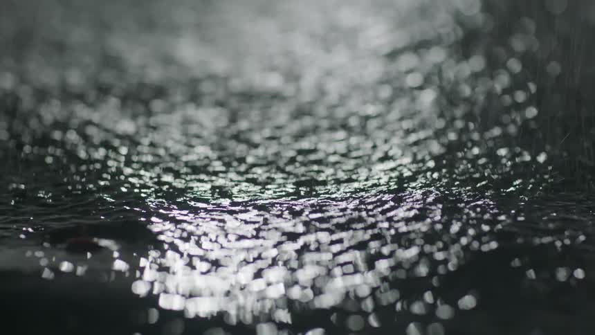 A fallen leaf floats in a puddle as rain falls down