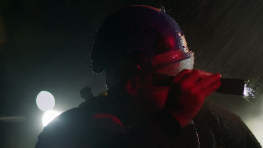 A first responder stands in the pouring rain and shines his flashlight in to the darkness as he searches