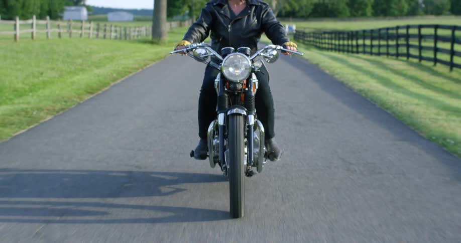 A woman is riding her motorcycle on the small road