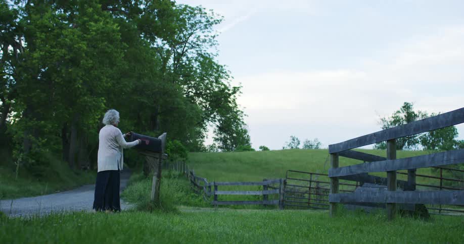 A elderly woman in a rural area puts an envelope in a mailbox