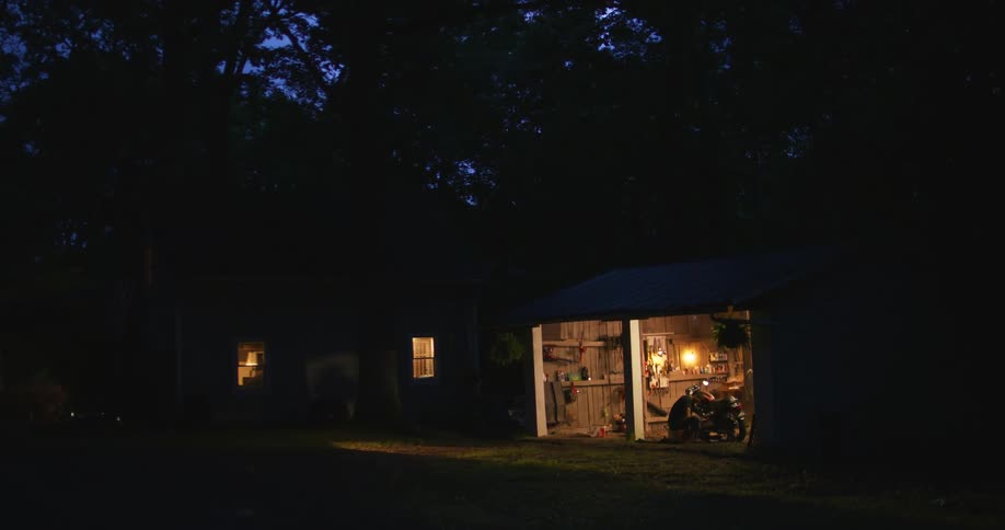 Man works on motorcycle using blowtorch in open garage at night