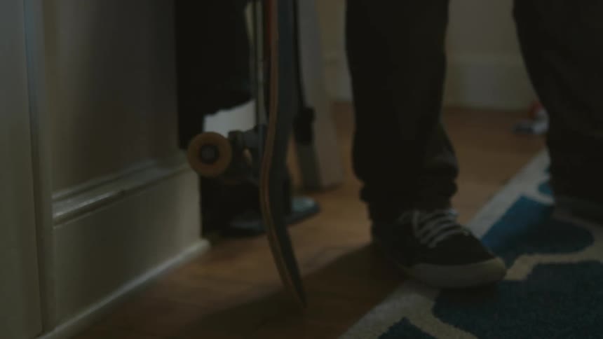 A person walking into a room and picking up a bottled water and a skateboard