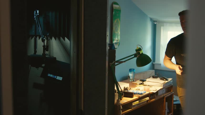 A man picks his laptop up from his desk and walks in to another room