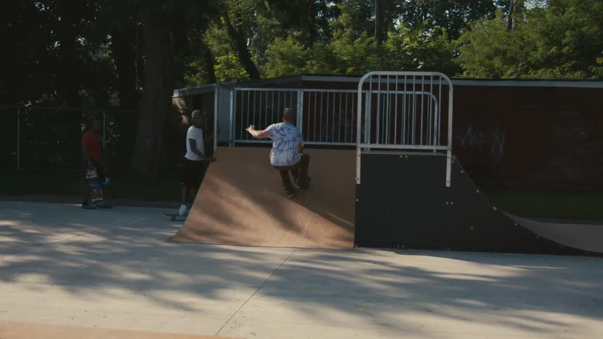 A man goes up a ramp on his skateboard in a park as two other men watch him