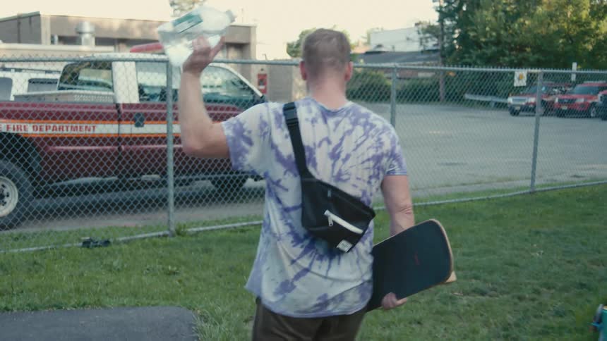 A man carries a skateboard and water jug as hes walking out of a public park