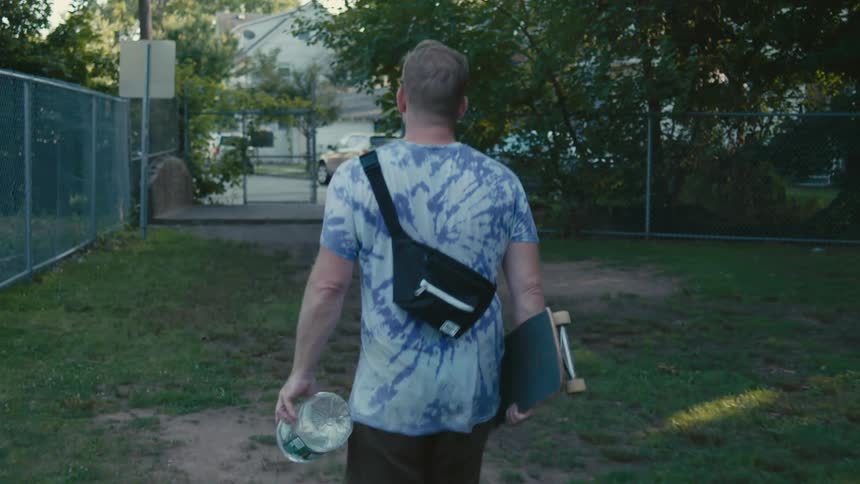 A man is walking while carrying his skateboard