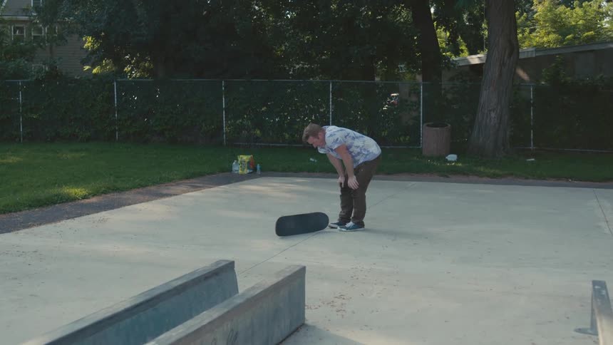 A man in a public park picks up his skateboard and walks away