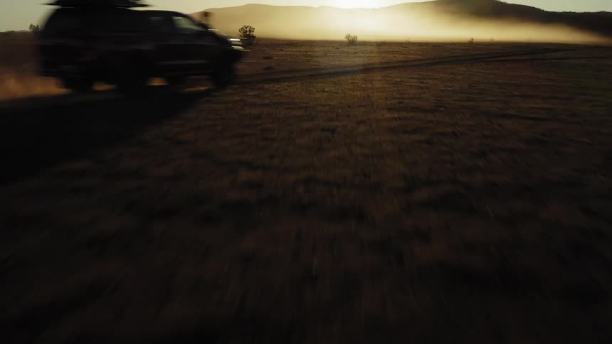 A vehicle drives over the field at sunrise