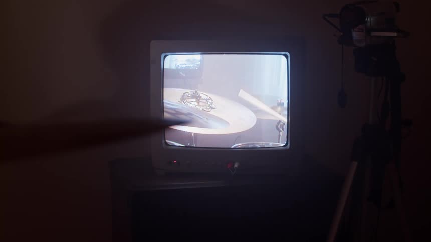 A television displaying a cymbal being hit by a drumstick in the dark