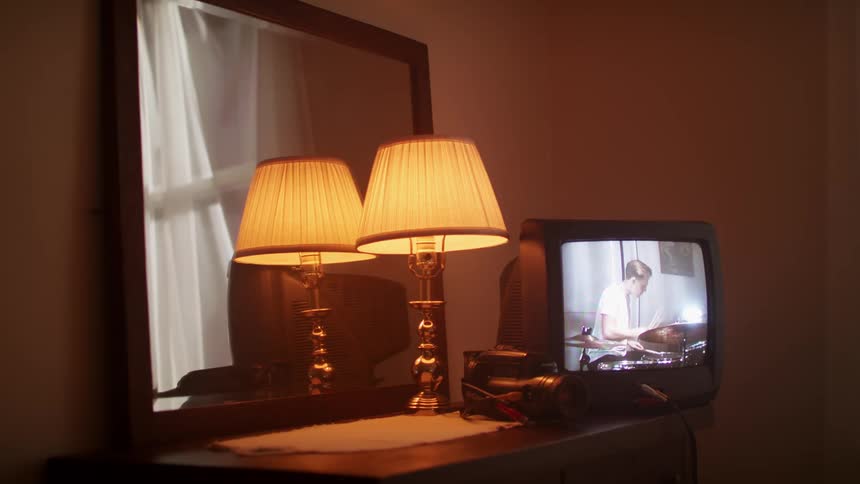 Television on dresser shows picture shot from camera of drummer playing drums
