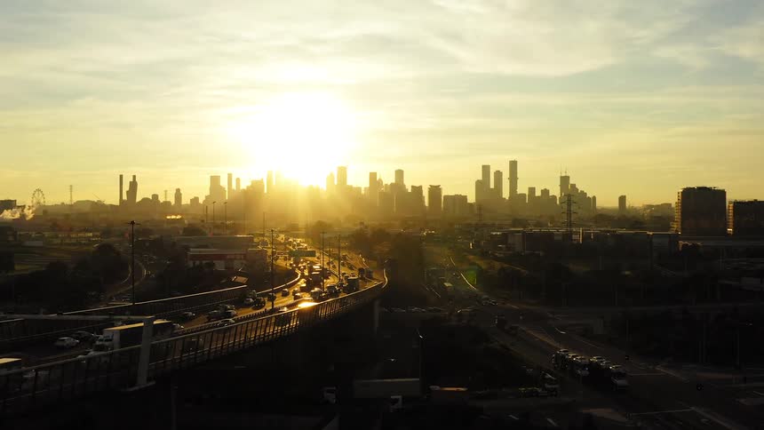 Aerial view of vehicles driving on highways and the sun setting behind the high rise buildings on the horizon