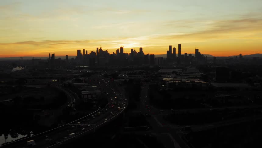 Traffic moves along a freeway on the outskirts of a city at sunset