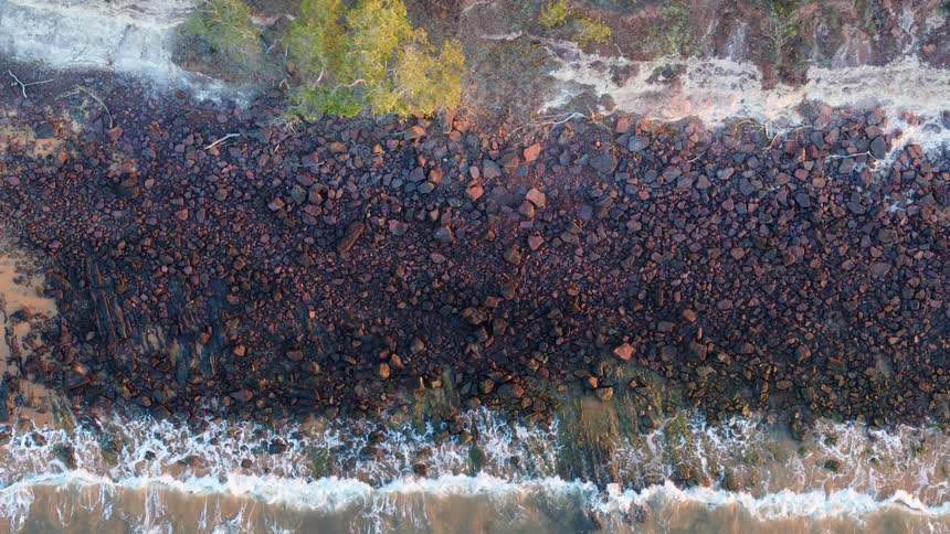 Aerial view of ocean waves breaking against the rocky shore