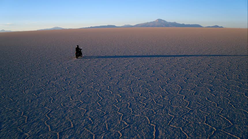Aerial view of a motorcyclist riding a motorcycle across the large desert