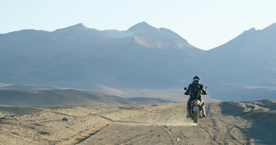 A person rides their motorcycle towards the mountains
