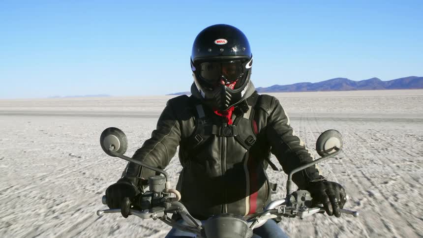 Motorcyclist with a helmet a black leather jacket and jeans rides a motorcycle across the large white sand desert