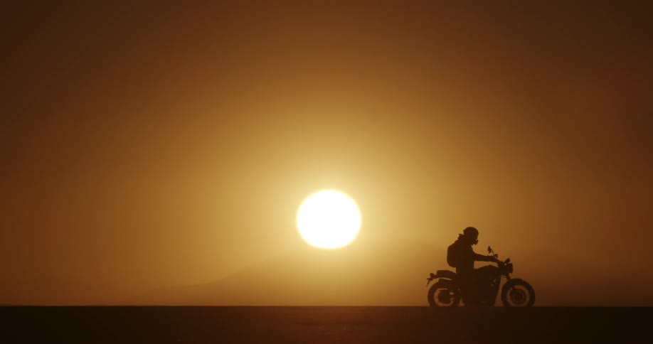 A motorcycle rider drives past hills at sunset