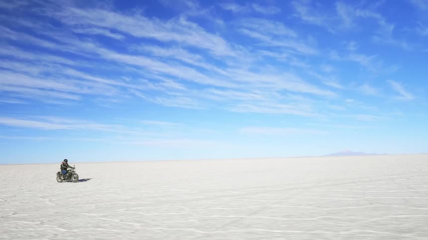 A person rides a motorcycle across a frozen arctic flatland on a sunny day