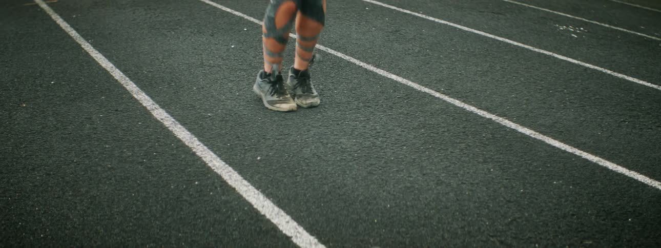 A woman with full leg tattoos jumps rope on an outside track