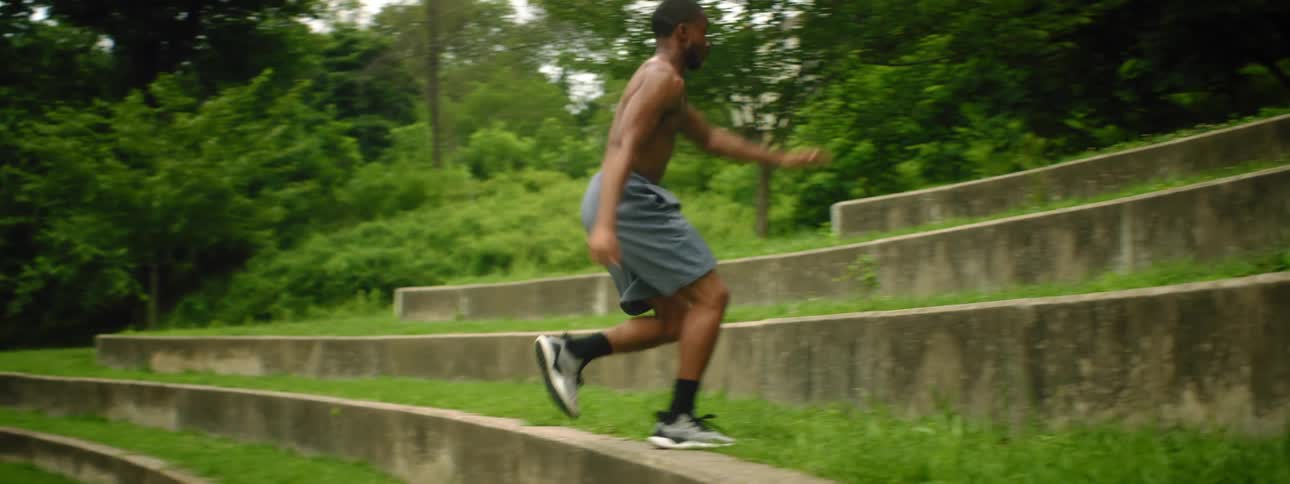 Topless man wearing shorts runs up wide tall terrace steps