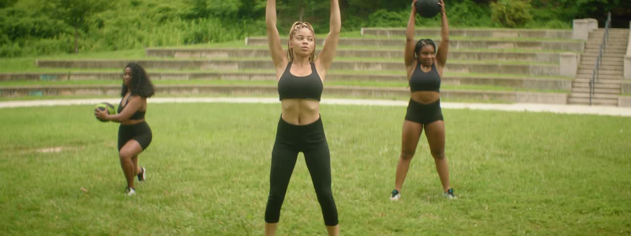 Three woman lifts weights and medicine balls in an exercise routine outdoors