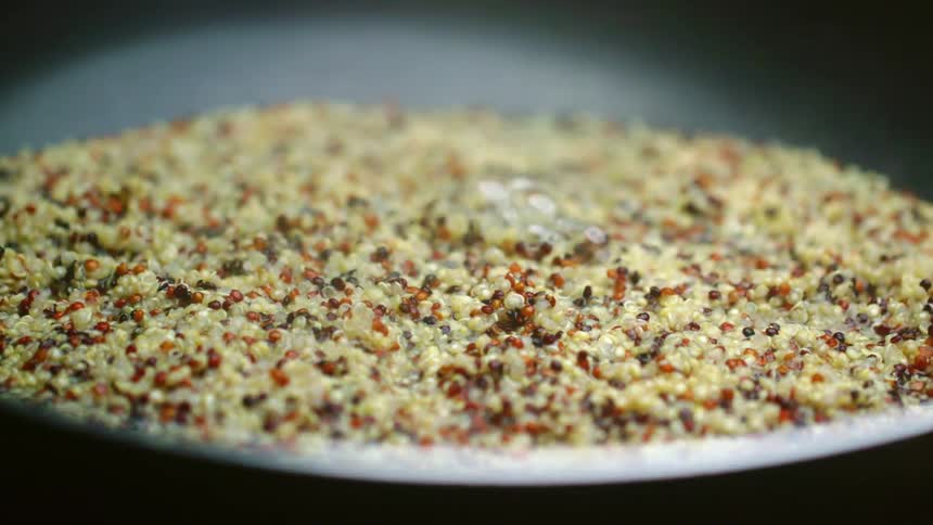 A cook gently pats quinoa with a wooden spoon as it boils and cooks in a nonstick pan