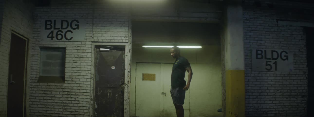 Young fit man wearing sports clothing stretches inside a dimly lit building