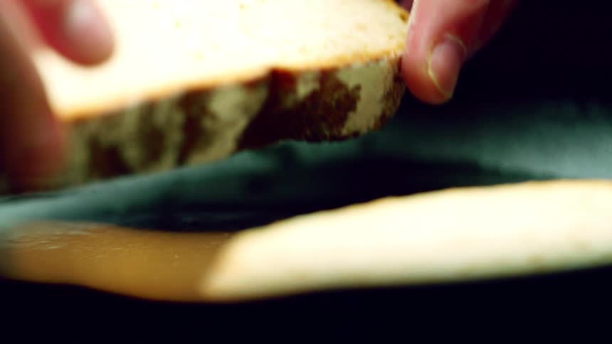 A person places a slice of bread on a cast iron pan