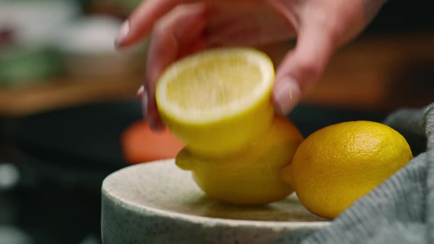 A woman picks up a lemon thats been sliced in half from a plate in her kitchen
