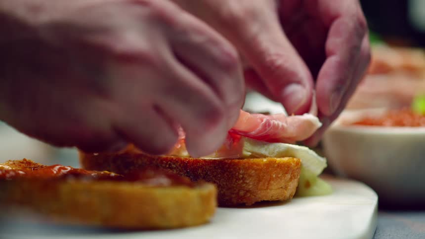 A man cooking puts meat on bread