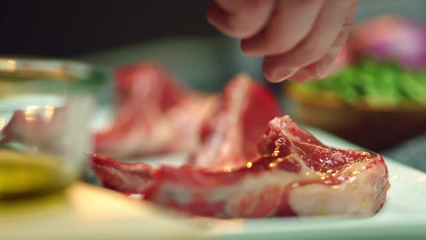 Person sprinkles salt on cuts of uncooked meat