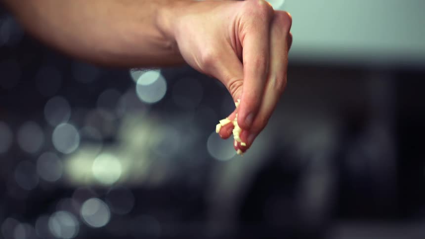 A person uses their hand to sprinkle shredded cheese into a glass bowl