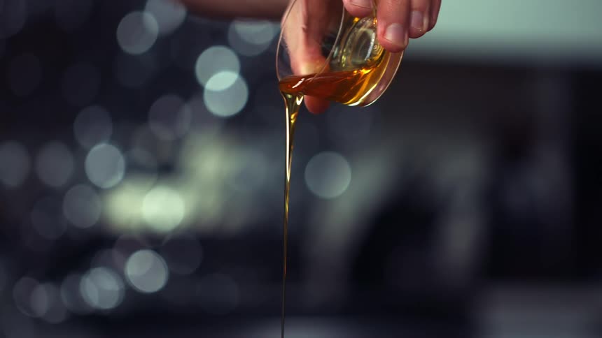 A young man at home pours honey as he cooks