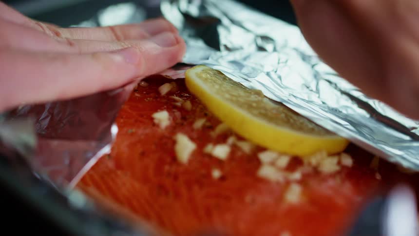 A cook wraps a seasoned salmon steak in foil