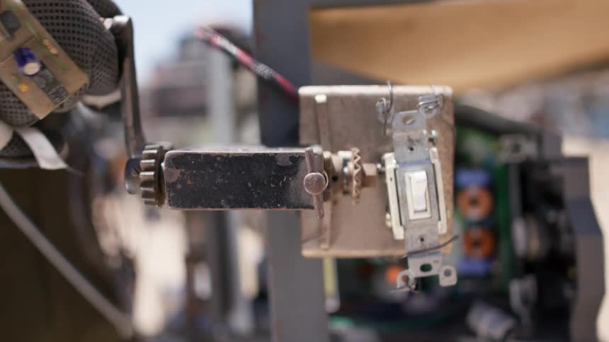 A person with gloves with wires turning on a switch and turning a lever