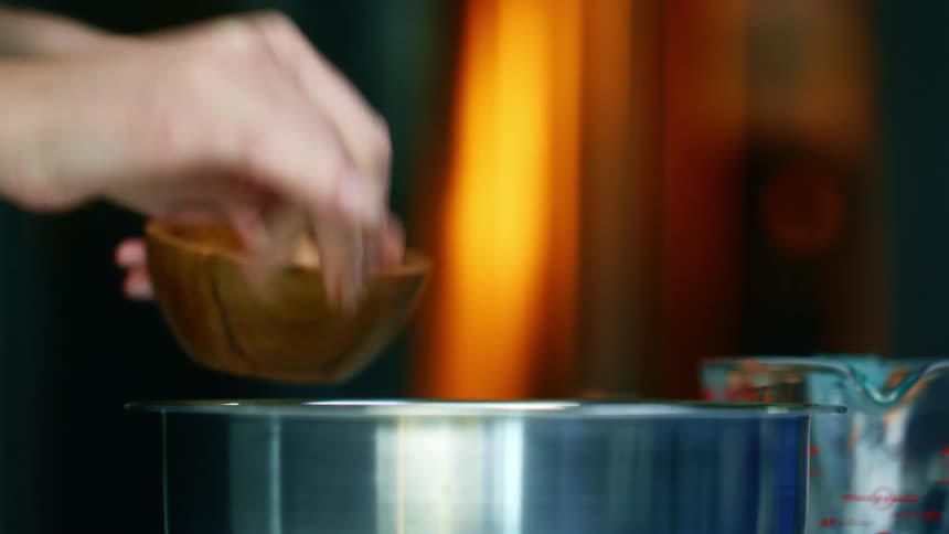 A person preparing food using a pot and spices with milk