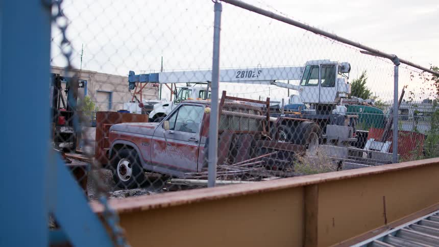 A fence next to vehicles with a building the sky and clouds in the background