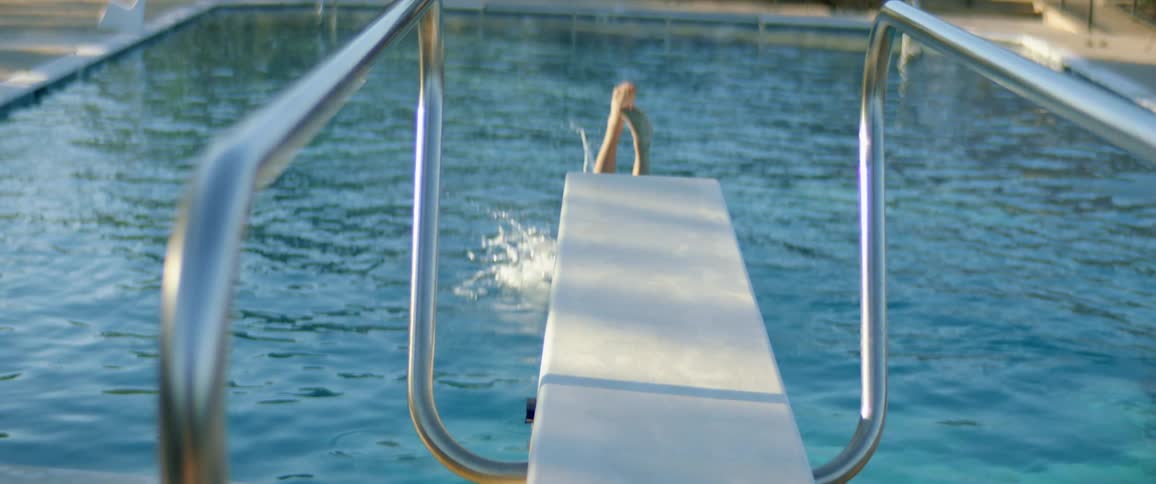 A female diver jumps off a low diving board into an outdoor pool