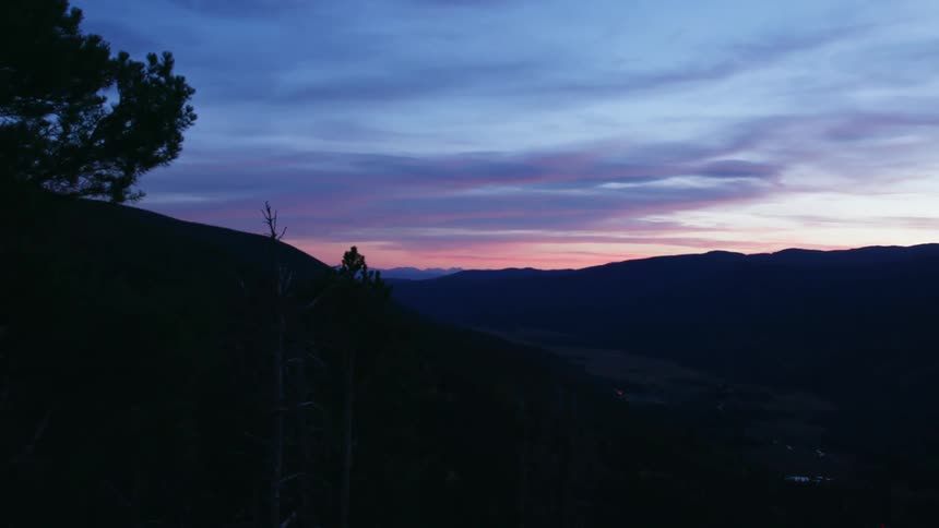 Person sits on mountainside high above valley at dawn