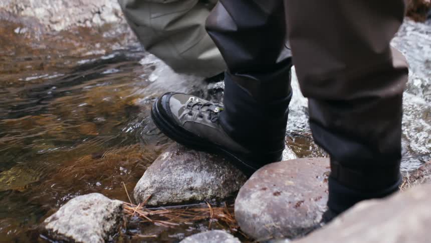 Two men stand on a river bank and then one man walks through the river