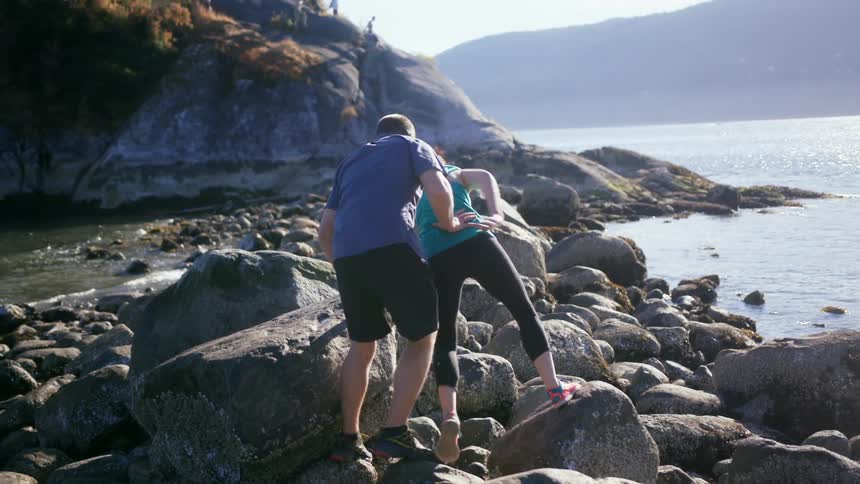 A woman raises her arms in victory after almost falling while walking on rocks next to the ocean