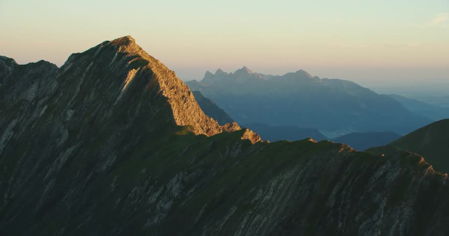 The sun rises and shines bright on a mountain range adjacent to the ocean